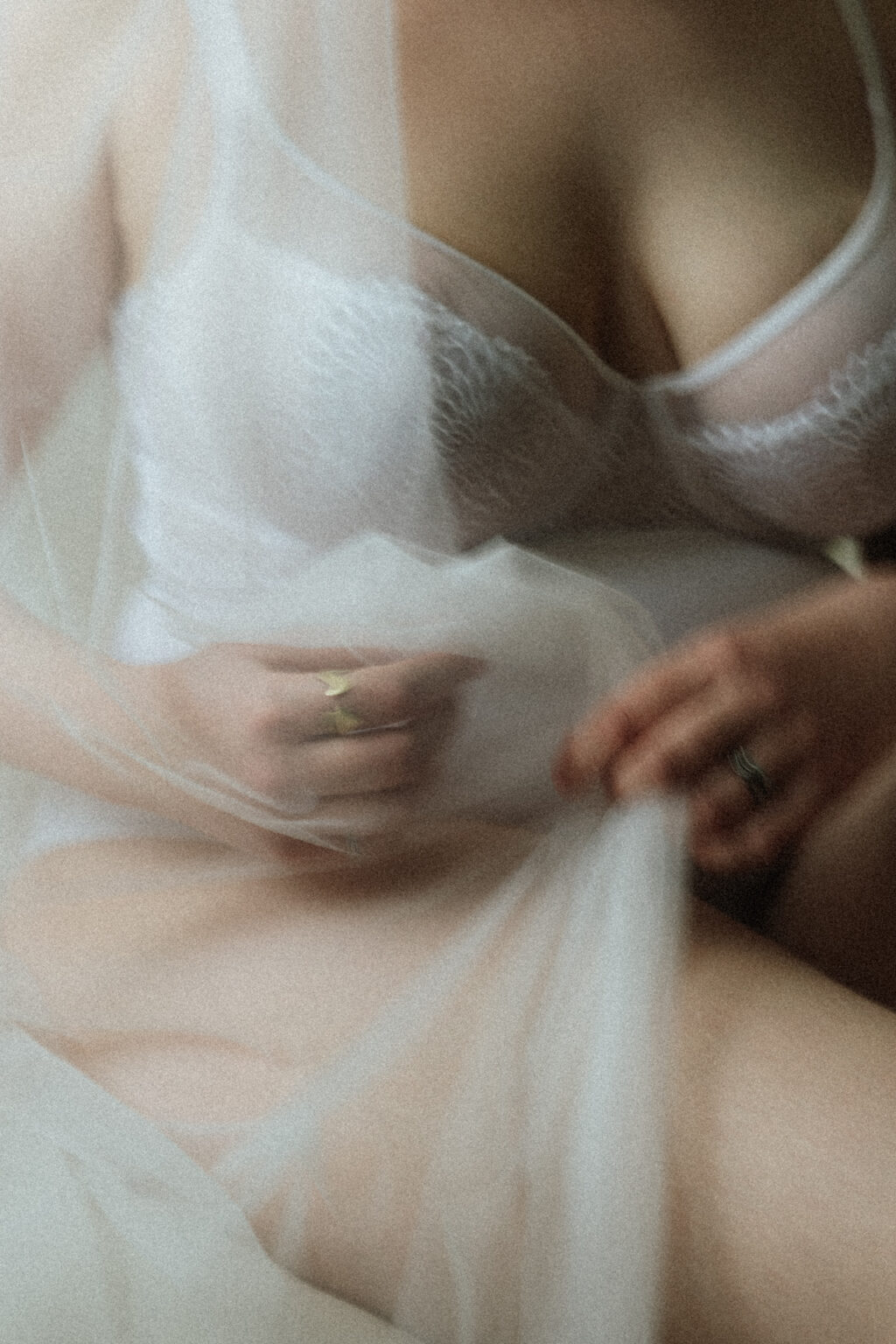 Séance boudoir de la mariée. Gros plan flou et délicat sur une mariée en lingerie blanche, enveloppée dans un voile transparent.