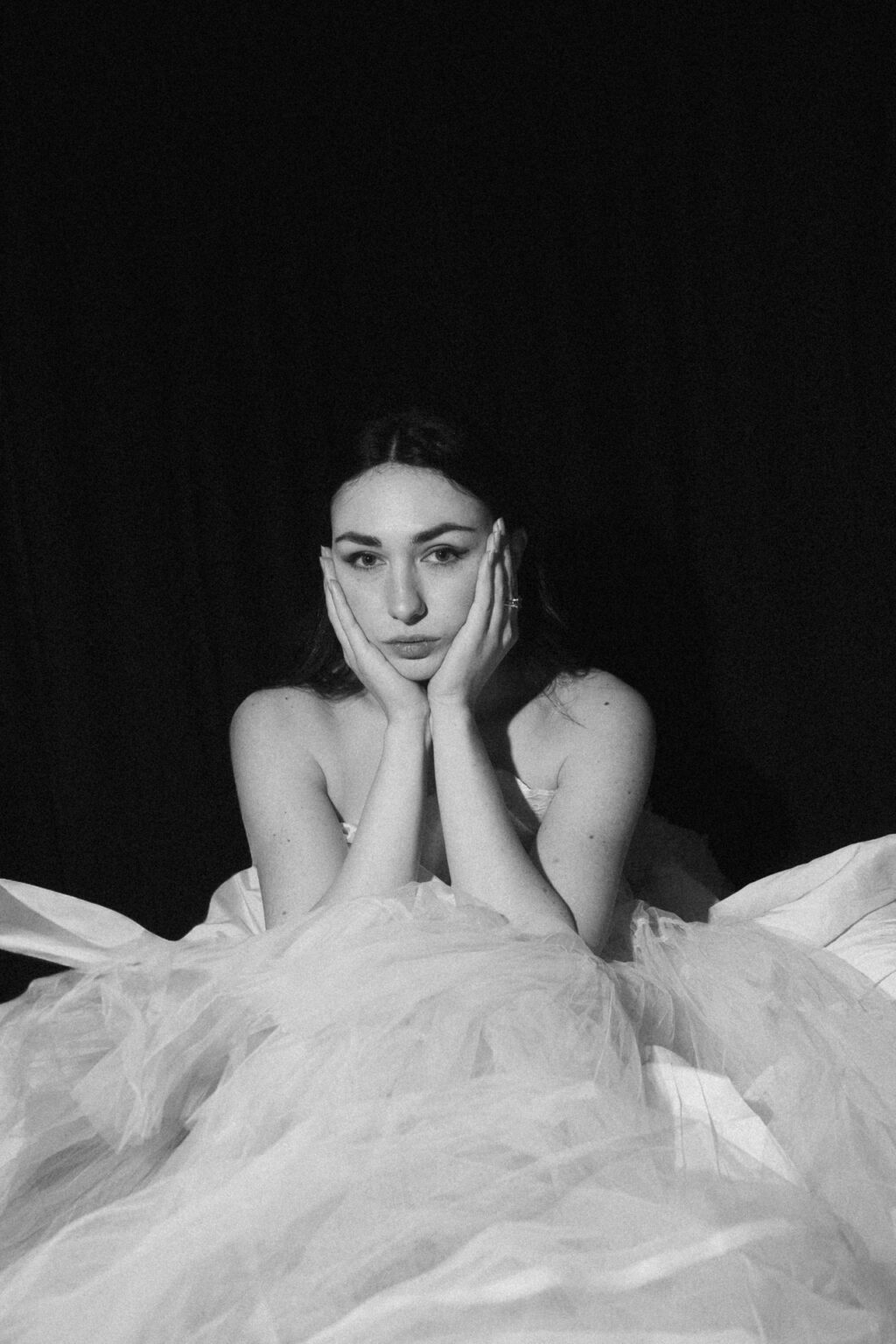 Portrait noir et blanc d’une mariée allongée dans son voile, dans une ambiance éditoriale. Pendant une séance boudoir de la mariée
