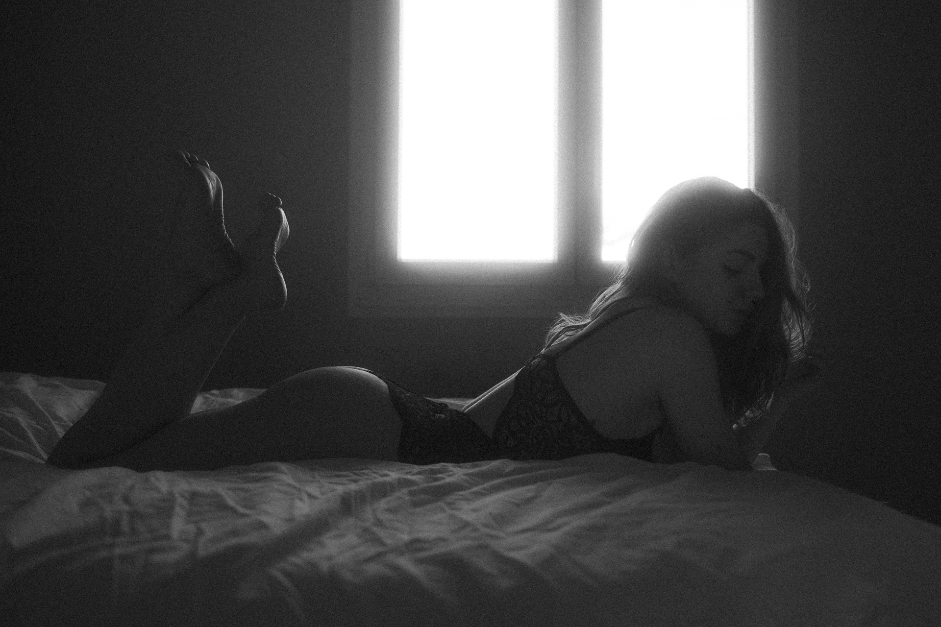 Séance boudoir en Moselle avec lingerie noire, femme allongée sur un lit dans un clair-obscur intimiste.